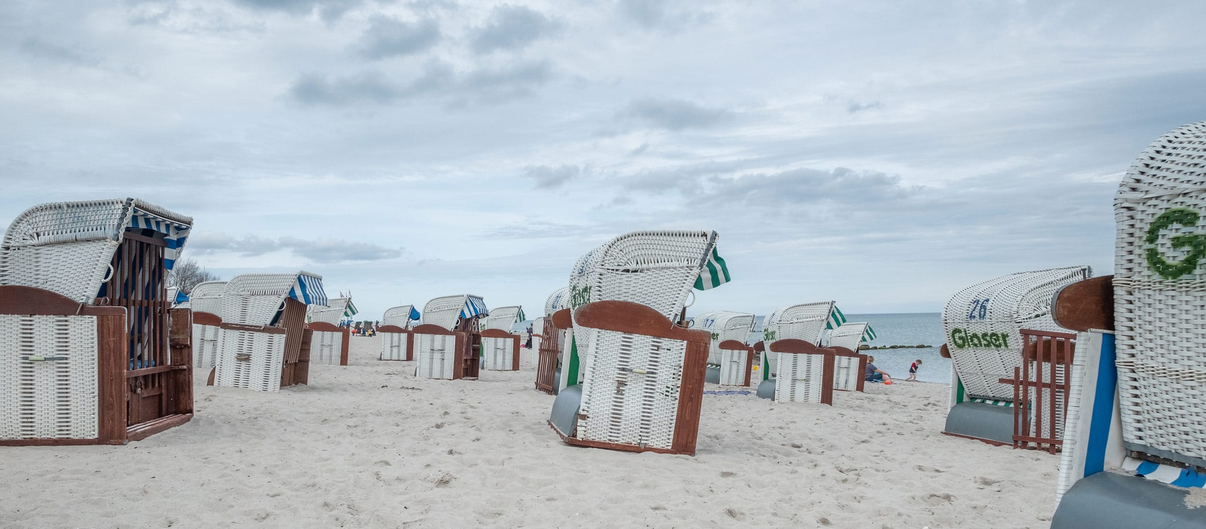 Strandansicht direkt bei der Ostseeklinik Grömitz mit typischen blau-weißen und grün-weißen Strandkörben an der Ostsee.