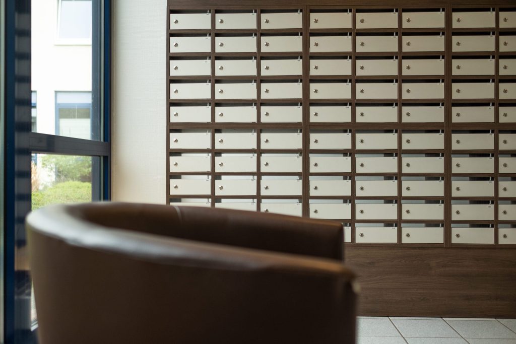 Eine Wand mit zahlreichen weißen Postfächern in einem dunklen Holzregal im Empfangsbereich der Ostseeklinik Grömitz, mit einem unscharfen braunen Ledersessel im Vordergrund
